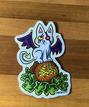 Load image into Gallery viewer, Sticker of a cat with bat wings on a pumpkin with 'INKSHIFT' branding on a wooden surface.