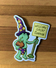Load image into Gallery viewer, Sticker of Speedo Frog holding a &#39;Welcome Great Pumpkin&#39; sign on a wooden surface
